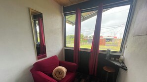 A room with a red armchair, a small table with a bottle, a mirror, and a window with curtains. - Poas Volcano Rooms  (Sabanilla)
