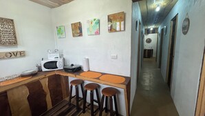 A kitchen with a microwave, toaster, and bar stools. There are wall decorations and a hallway leading to another room. - Poas Volcano Rooms  (Sabanilla)