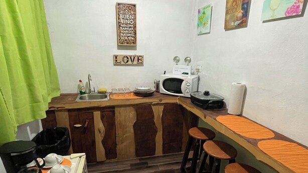 A compact kitchen with a wooden island, bar stools, a microwave, and a sink. - Poas Volcano Rooms  (Sabanilla)