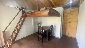 A room with a wooden staircase leading to a lofted sleeping area, a dining table with chairs, and a door. - Poas Volcano Rooms  (Sabanilla)