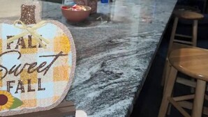 Eine Küche mit Marmorarbeitsplatte, Holzschränken und einem dekorativen Schild mit der Aufschrift 'FALL Sweet FALL'.