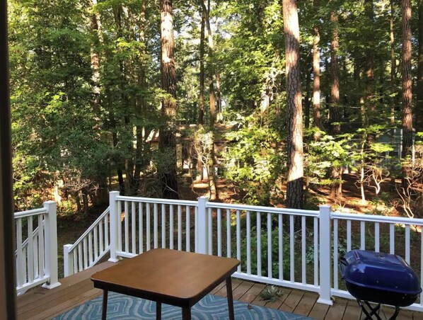 A wooden deck with a white railing, a table, and a barbecue grill.