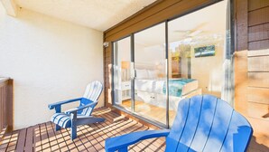 A balcony with two blue Adirondack chairs, a wooden floor, and a view of a bedroom with a bed and a TV. - Sea Me 9E–Close to Beach–Sleeps 6 (Panama City Beach)