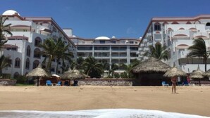 Un resort con varias edificaciones blancas, palmeras y sombrillas de techo de paja en la playa.