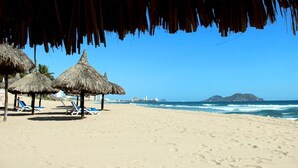 Una playa con sombrillas de paja, tumbonas y una vista despejada del océano y unas islas distantes.