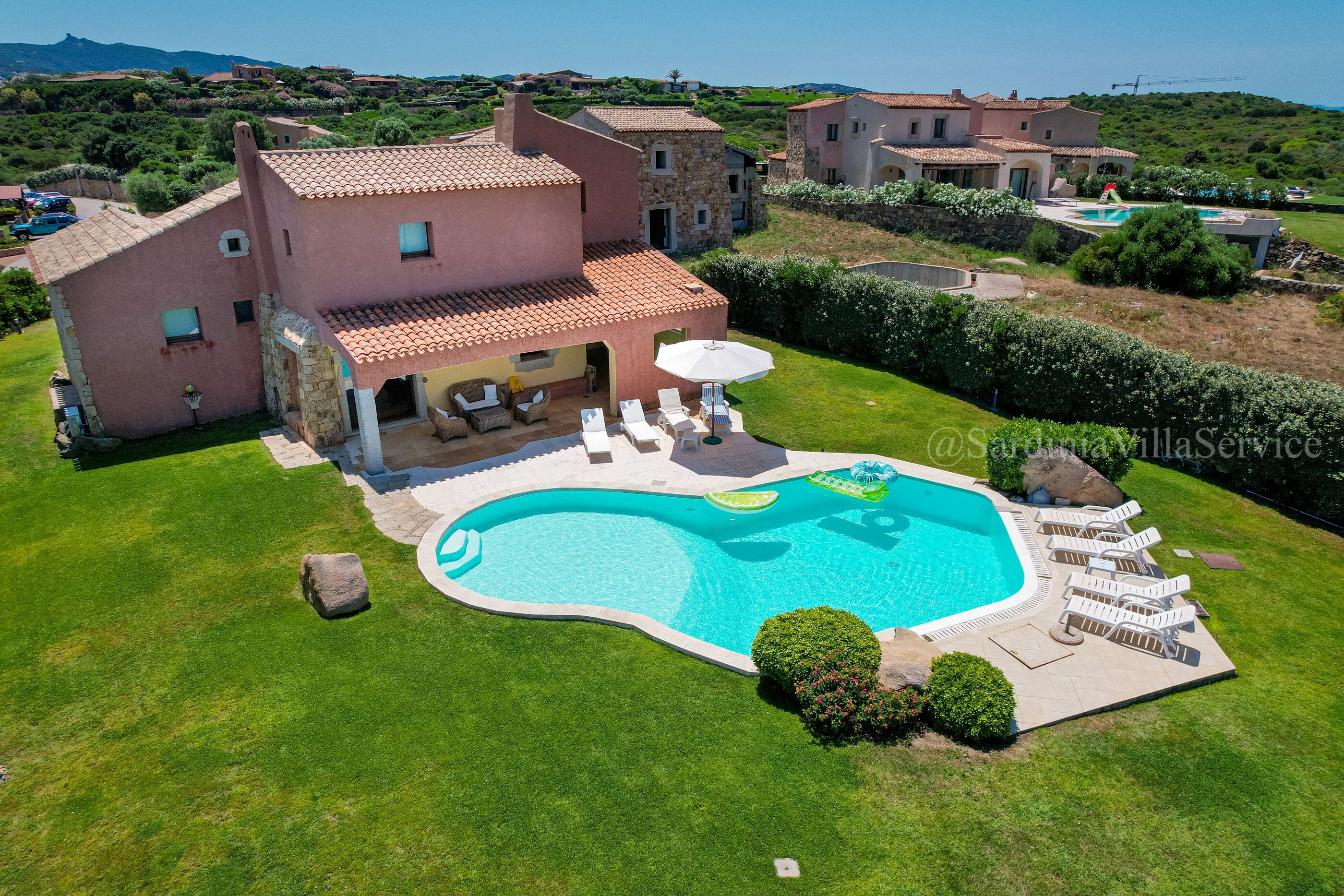 A villa with a swimming pool, outdoor seating, and a view of the surrounding landscape.