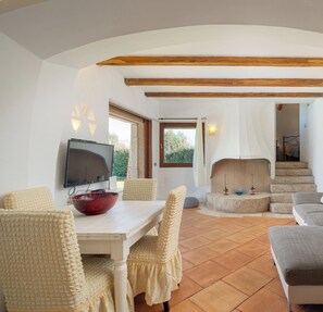 Un salón amplio con una mesa blanca, sillas color beige, un sofá gris y una chimenea.