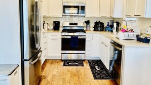 A modern kitchen with white cabinets, stainless steel appliances, and a wooden floor.
