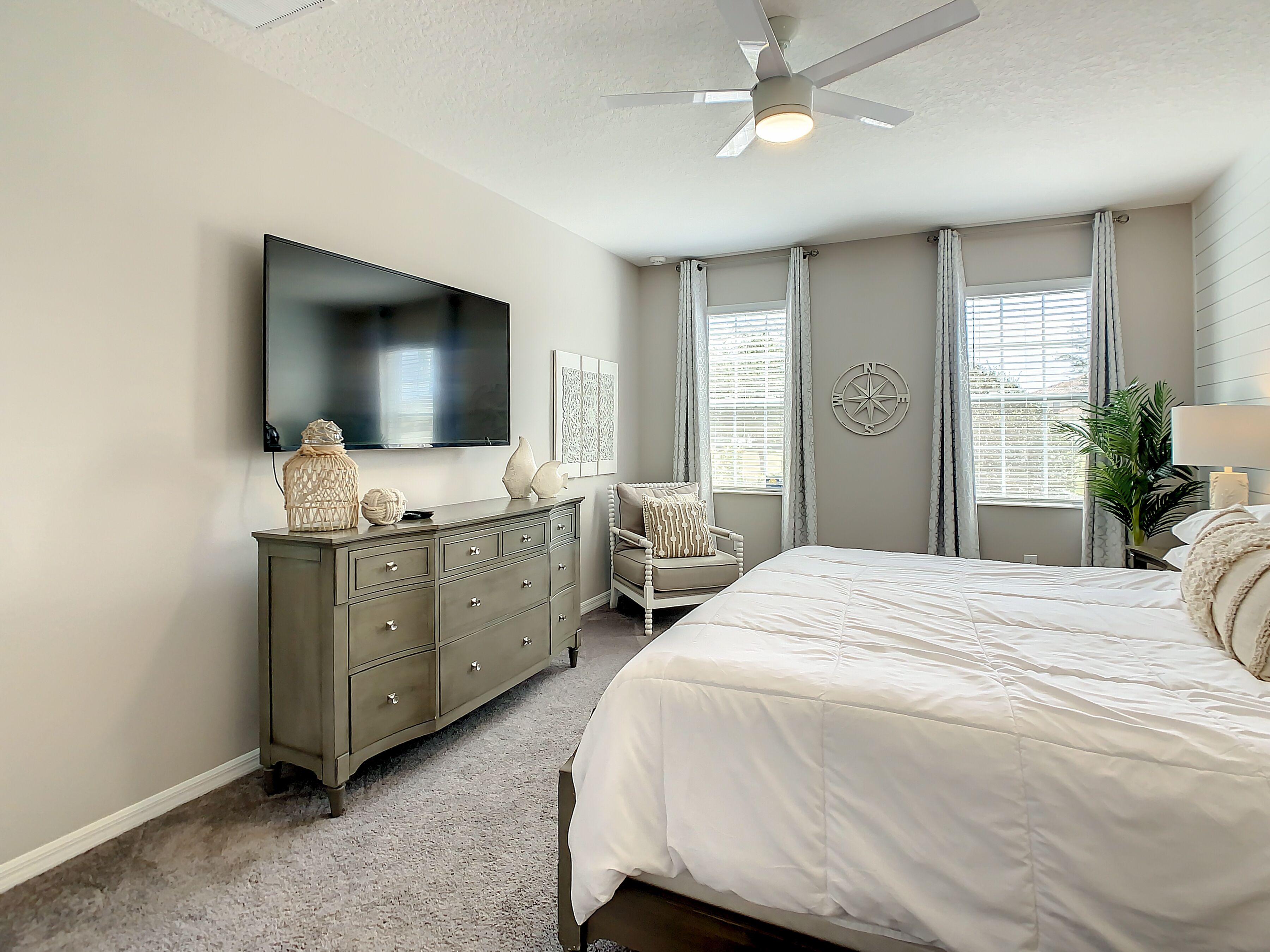 A bedroom with a bed, dresser, TV, and a ceiling fan.