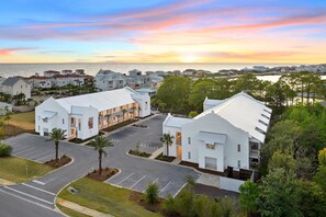 Stunning coastal residence with a gabled roof and central courtyard, surrounded by a parking lot and palm trees.