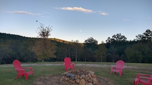Un campeggio con un braciere circondato da sedie rosse e una collina boscosa sullo sfondo.