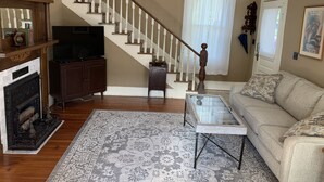 A living room with a staircase, a fireplace, a television, a sofa, and a coffee table. - Historic Murphy's House (St. Augustine)