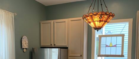 A kitchen with a stainless steel refrigerator, a built-in dishwasher, a sink, and a window with a stained glass design.