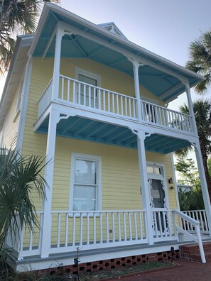 Une maison à deux étages avec une façade jaune, des ornements blancs et un toit bleu.