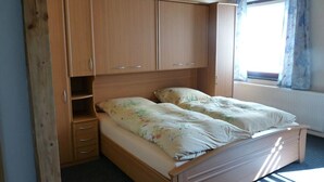 A single bed with a floral bedspread, wooden wardrobe, and a window with curtains. - Fair guests Harz visitors Bike - and Outdoorpark Bad Salzdetfurth (Bockenem)