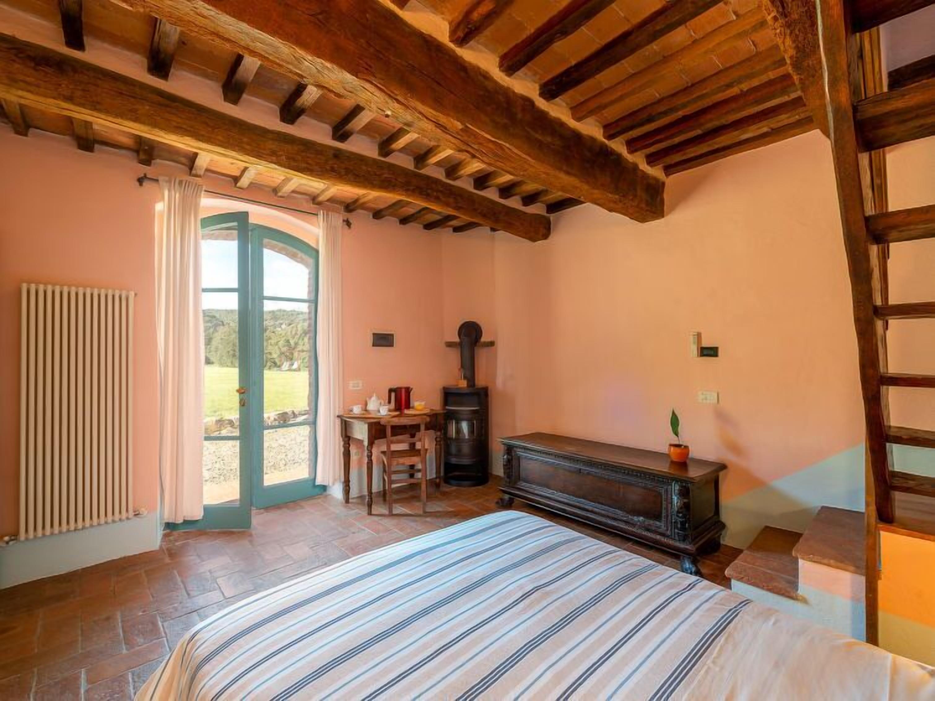 Ein Schlafzimmer mit Bett, Holzboden, Heizkörper, Kamin und Blick durch eine offene Tür.