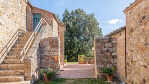 A stone building with a staircase leading to a door, surrounded by potted plants and a grassy courtyard. - Podere Vignali by Interhome (Pari)