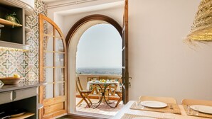 A dining area with a view of the sea, featuring a table set with plates and cutlery, and a wooden door leading to an outdoor seating area. - Mas Cusi (Palau-Saverdera)
