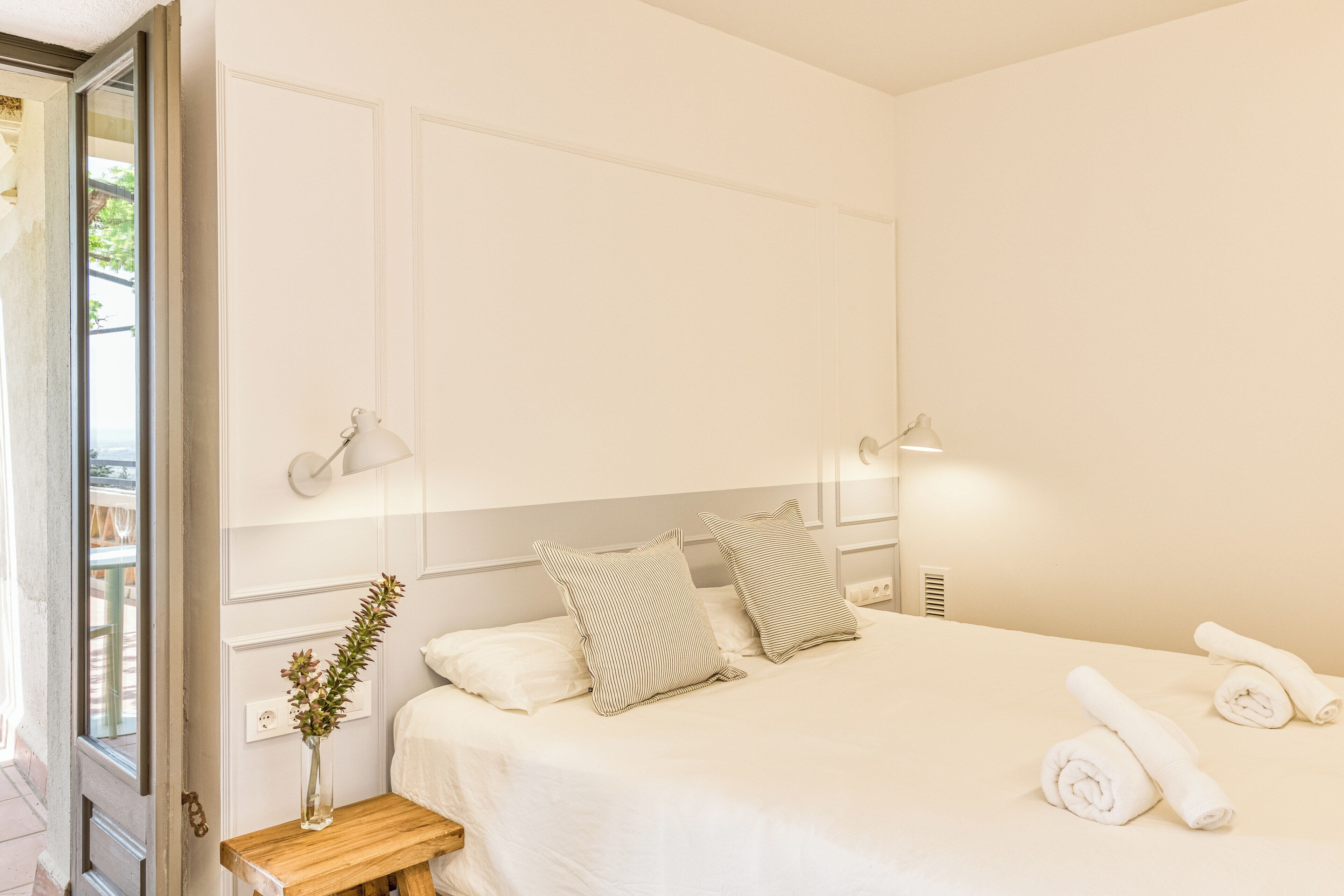 Un lit bien fait, avec des oreillers, une table de chevet ornée d’un vase et des serviettes pliées posées sur le lit.