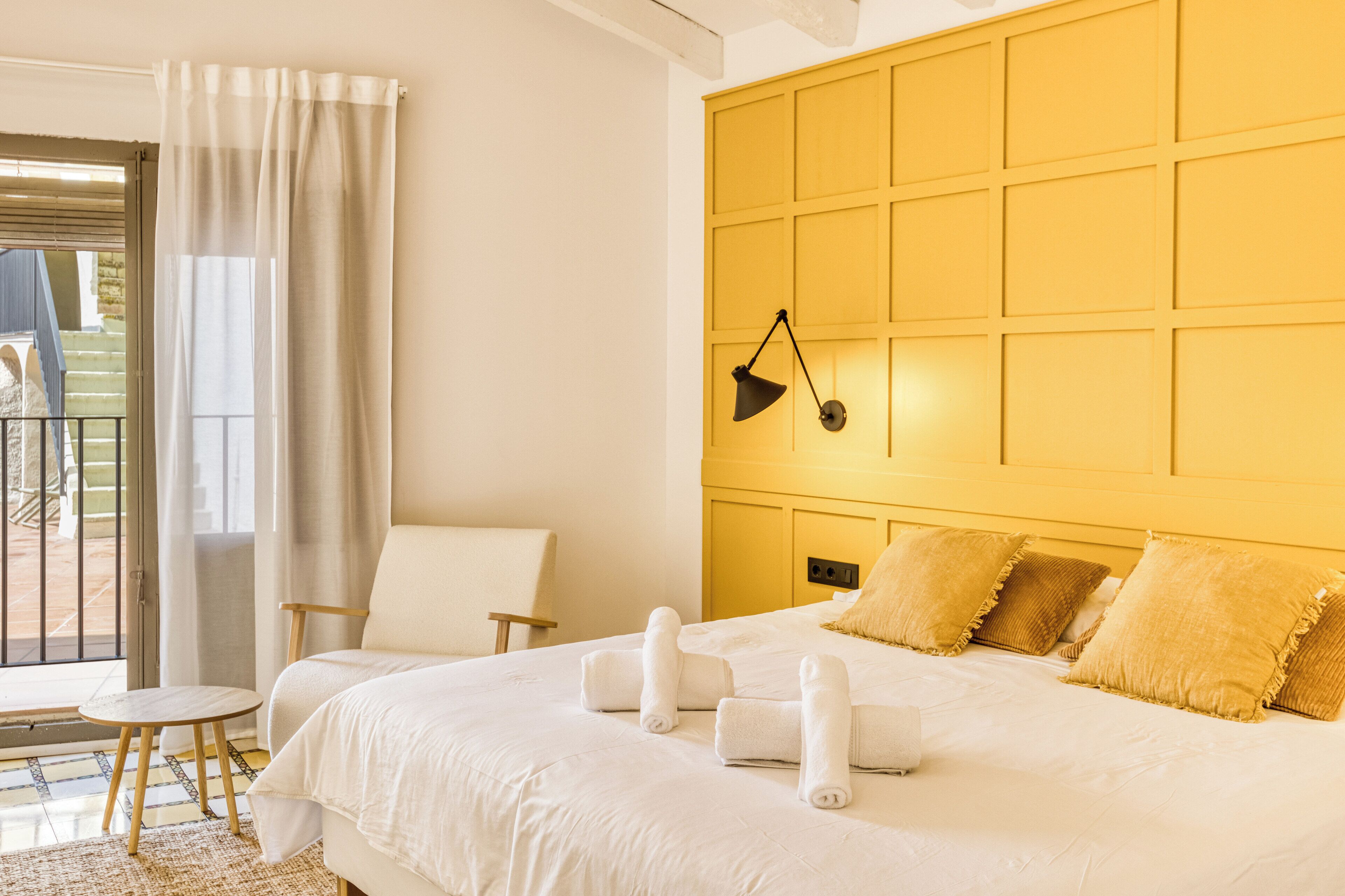 Une chambre d’hôtel avec un grand lit, une chaise, une petite table et une vue sur l’extérieur, visible à travers une porte vitrée.
