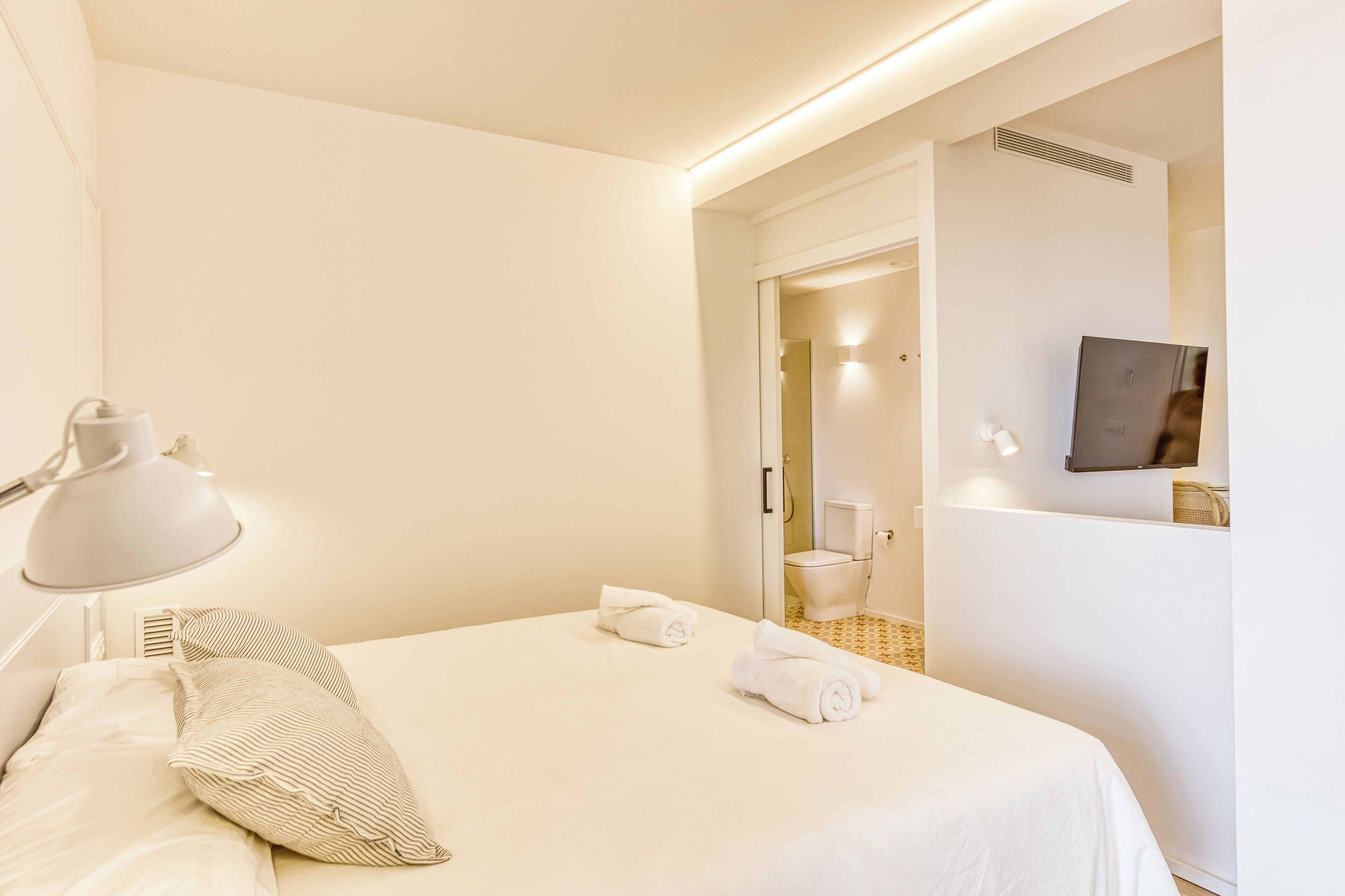 A hotel room with a neatly made bed, a bedside lamp, and a wall-mounted TV.