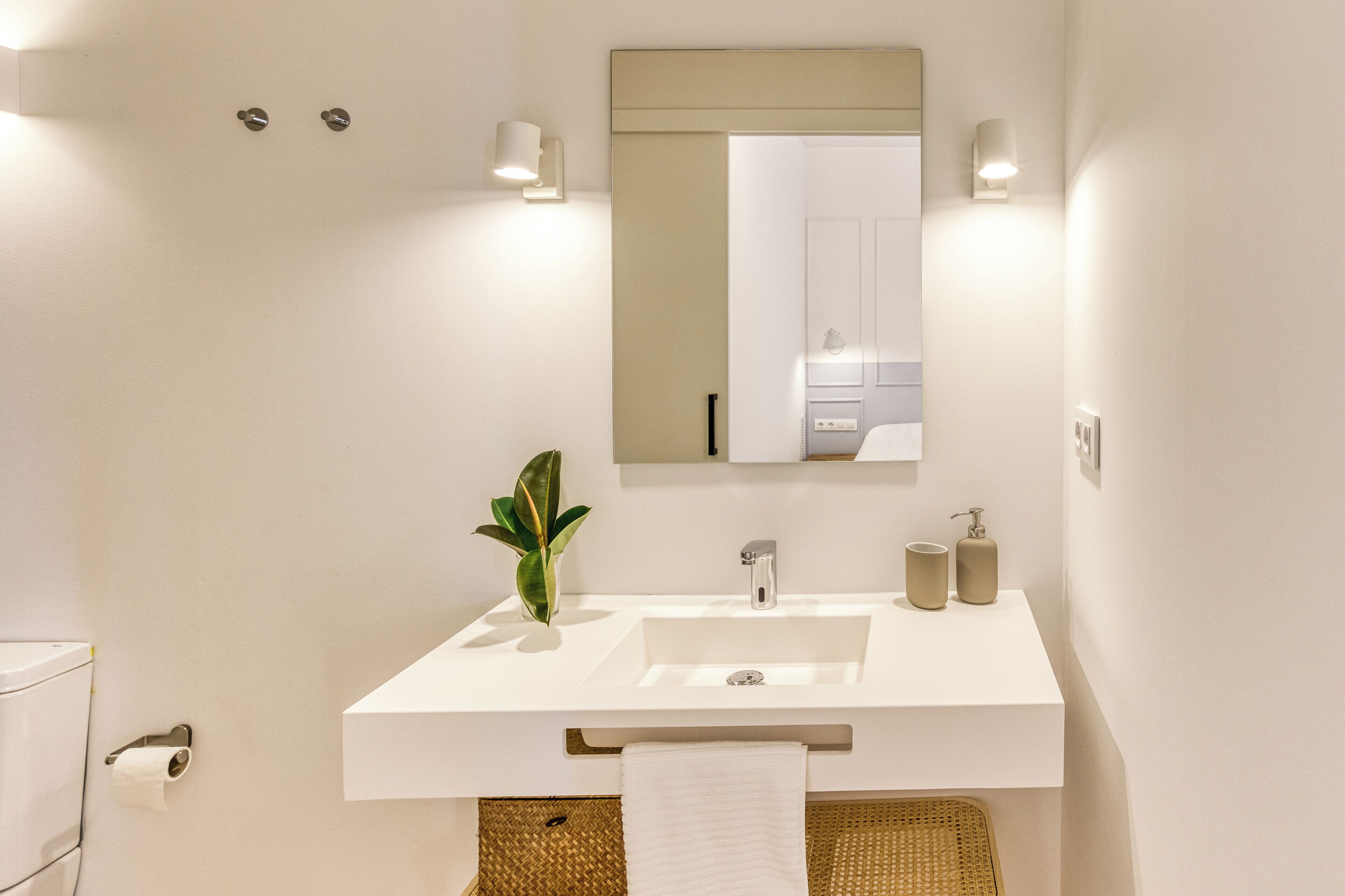 Une salle de bain moderne avec un lavabo blanc, un miroir et deux appliques murales.