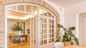 A room with a large arched doorway leading to another space, a wooden table, a chair, and a potted plant. - Mas Cusi (Palau-Saverdera)