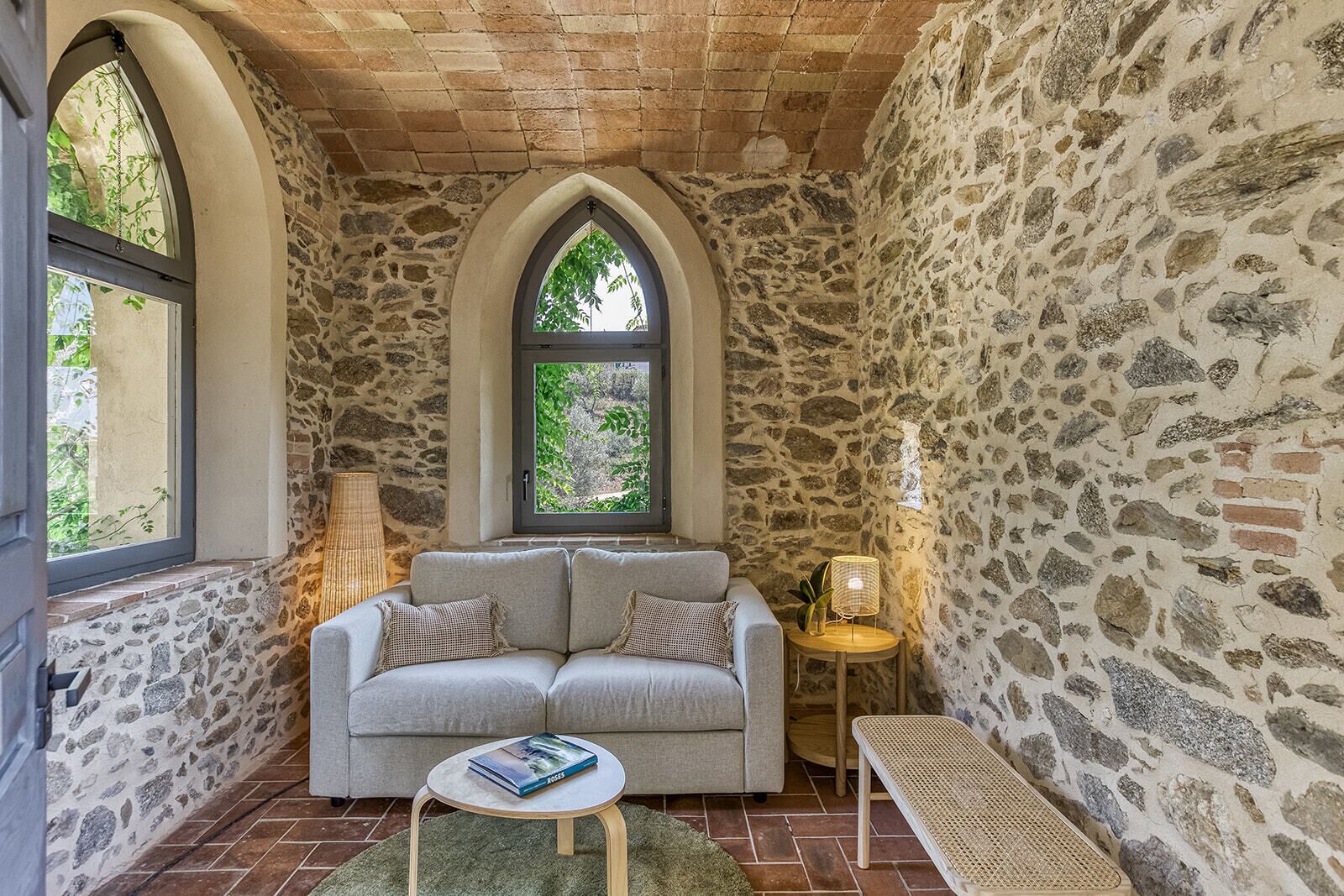Una habitación acogedora con pared de piedra, ventana con vistas a la vegetación, un sofá, una mesita y un banco.