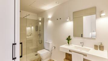 A modern bathroom with a glass-enclosed shower, a white toilet, a sink with a mirror, and a patterned floor.