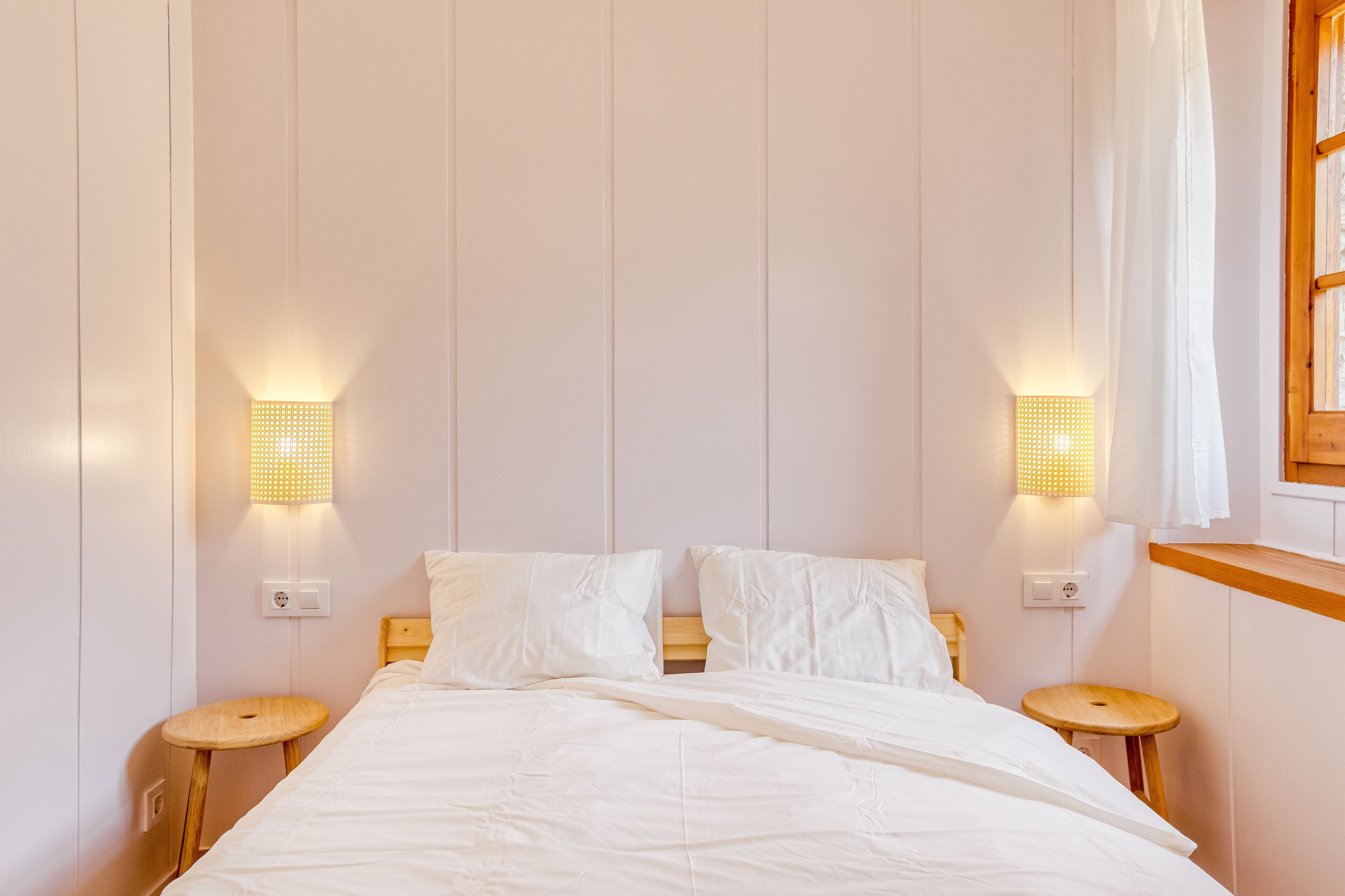 A neatly made bed with white linens, two bedside tables, and wall-mounted lamps.