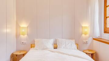 A neatly made bed with white linens, two bedside tables, and wall-mounted lamps.