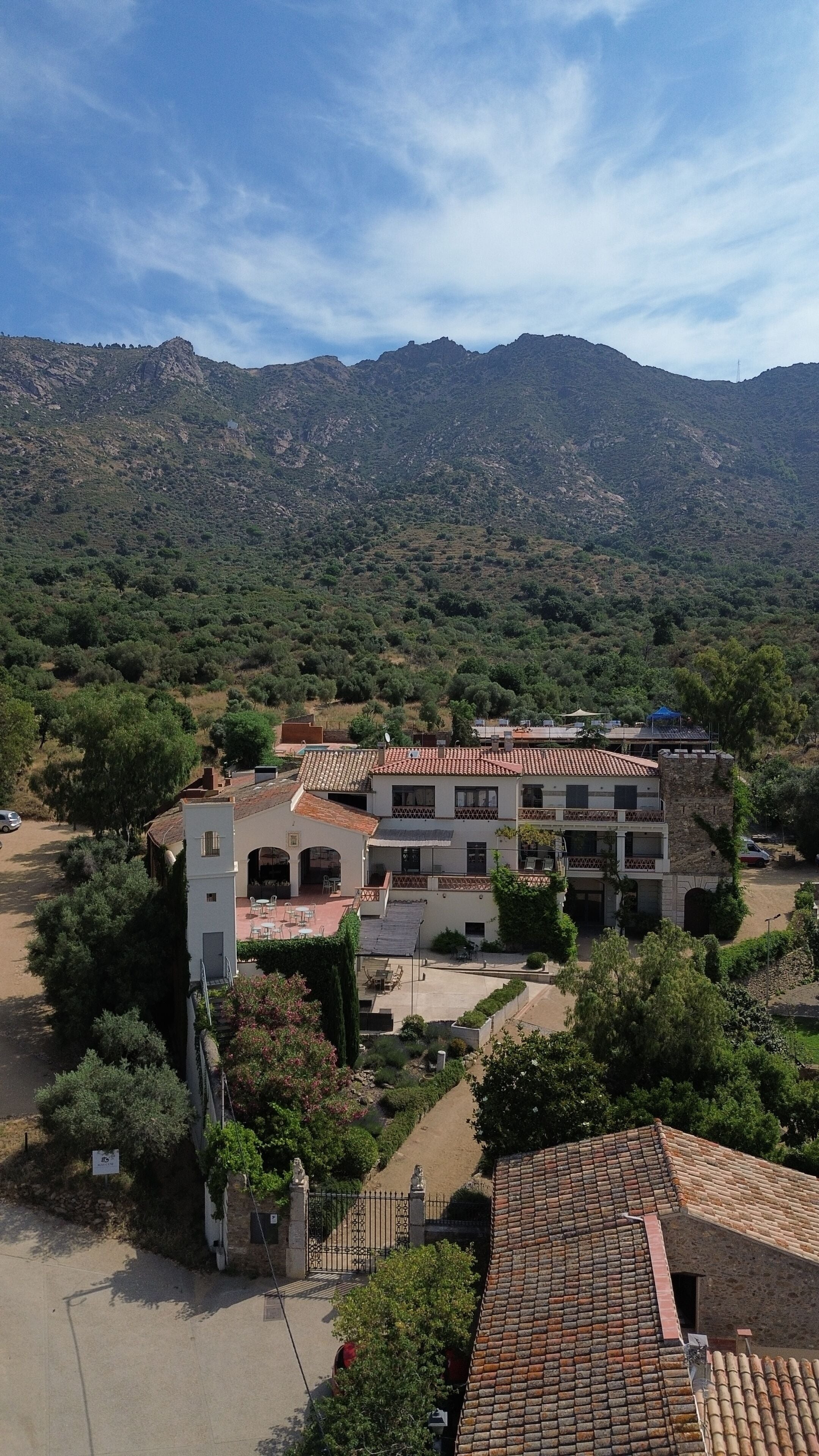 A building with a tiled roof, surrounded by greenery and mountains in the background.