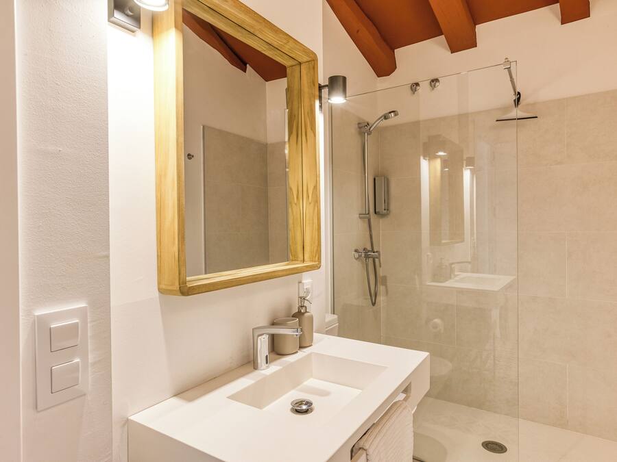 Un baño moderno con un lavabo blanco, un espejo grande y una cabina de ducha con paredes de cristal.