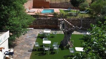 Un espace piscine agrémenté de chaises longues et de tables, entouré d’un mur de pierre et de verdure, avec des montagnes en toile de fond.