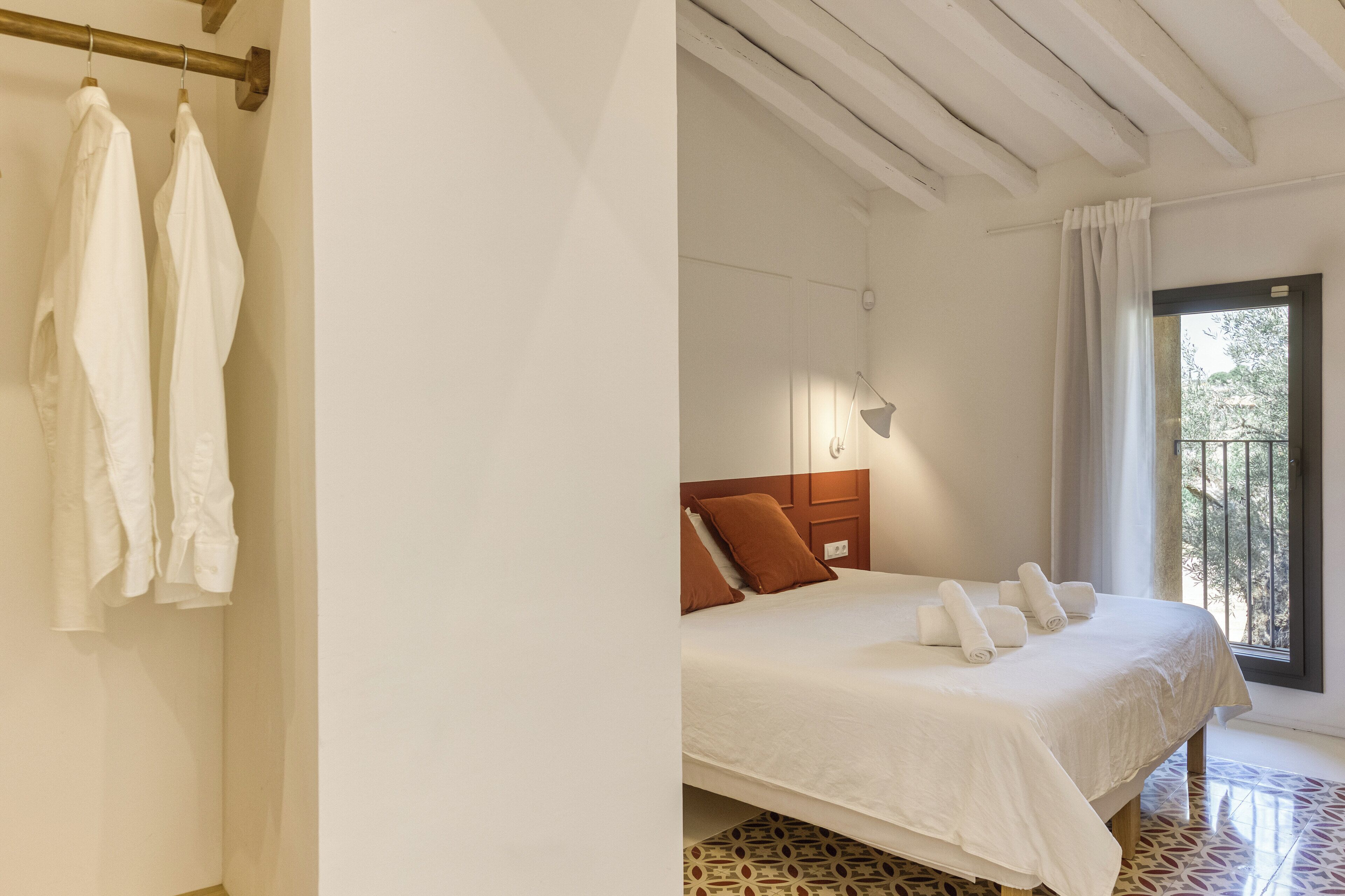 Un dormitorio con cama, cabecero de madera, ventana con vistas y suelo estampado.