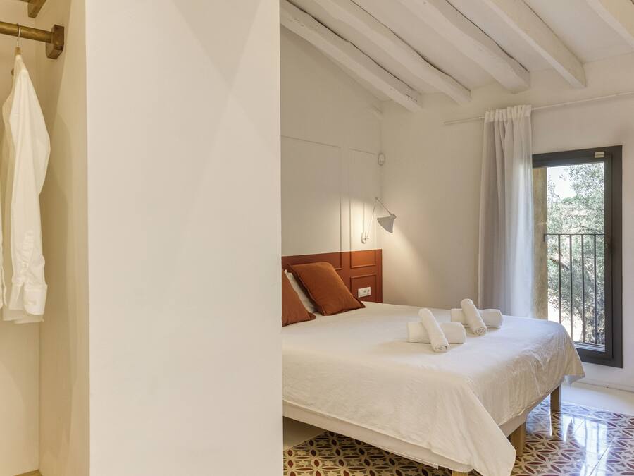 Un dormitorio con cama, cabecero de madera, ventana con vistas y suelo estampado.