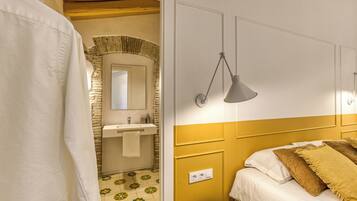 A bedroom with a bed, a bedside lamp, a bathroom with a sink and mirror, and a shower curtain.