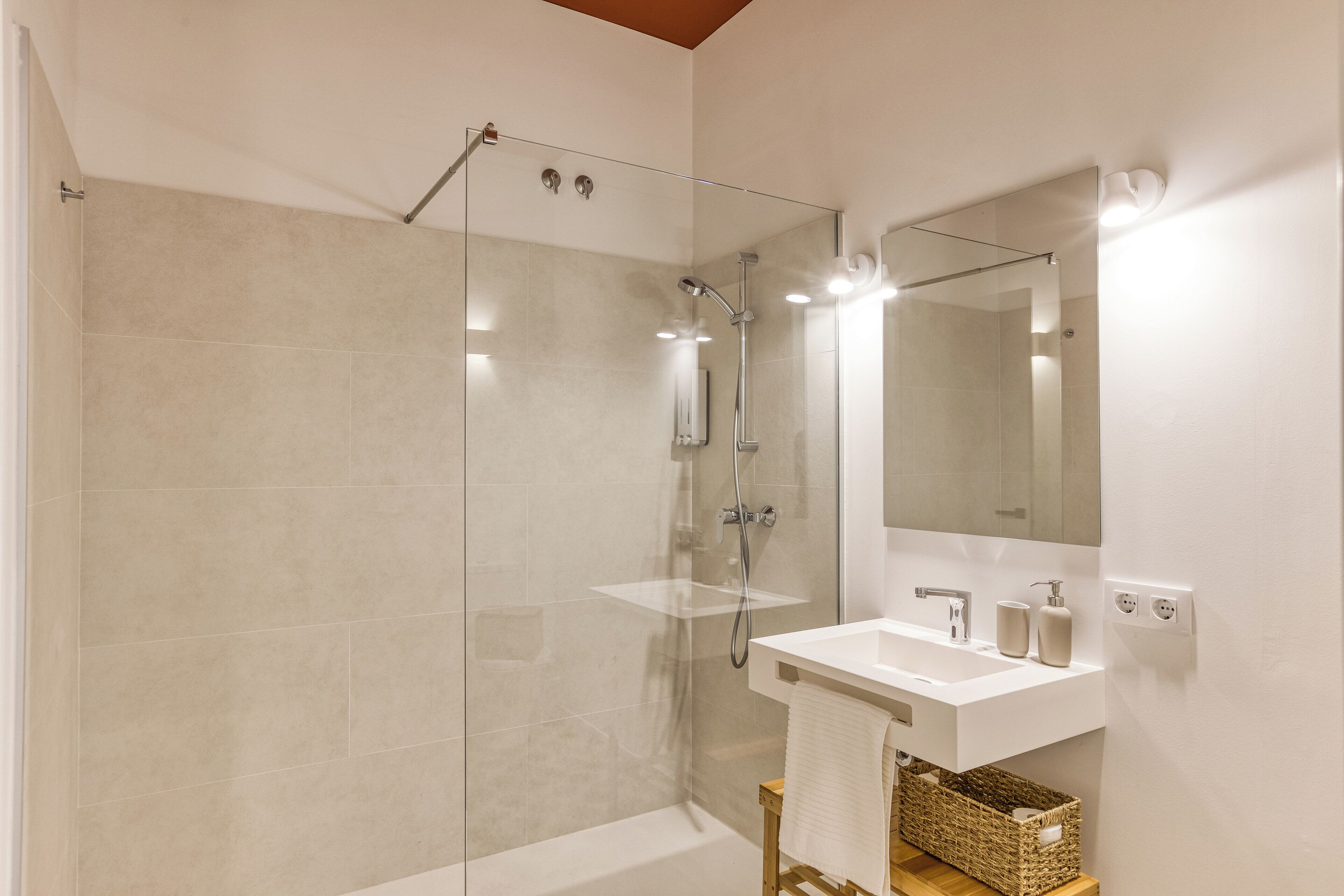 Un baño moderno con ducha envuelta en vidrio, un lavabo blanco y un espejo grande.