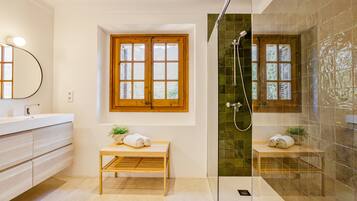 Un baño moderno con tocador de madera, un banco, un espejo grande, una ventana y zona de ducha con paredes de vidrio.