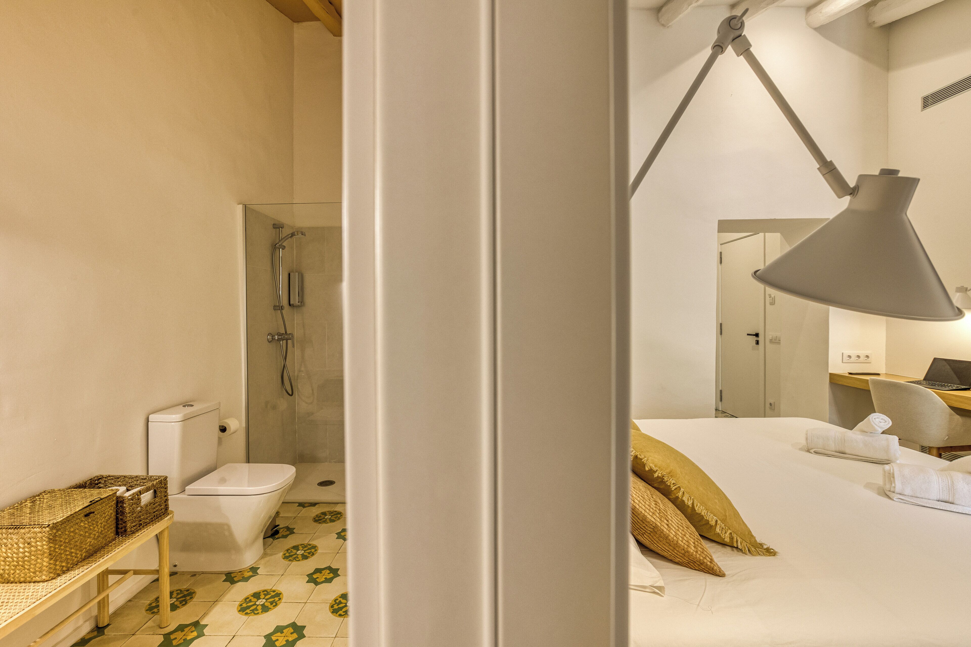 Habitación de hotel con ducha, inodoro, cama con almohadas y escritorio con una computadora portátil.
