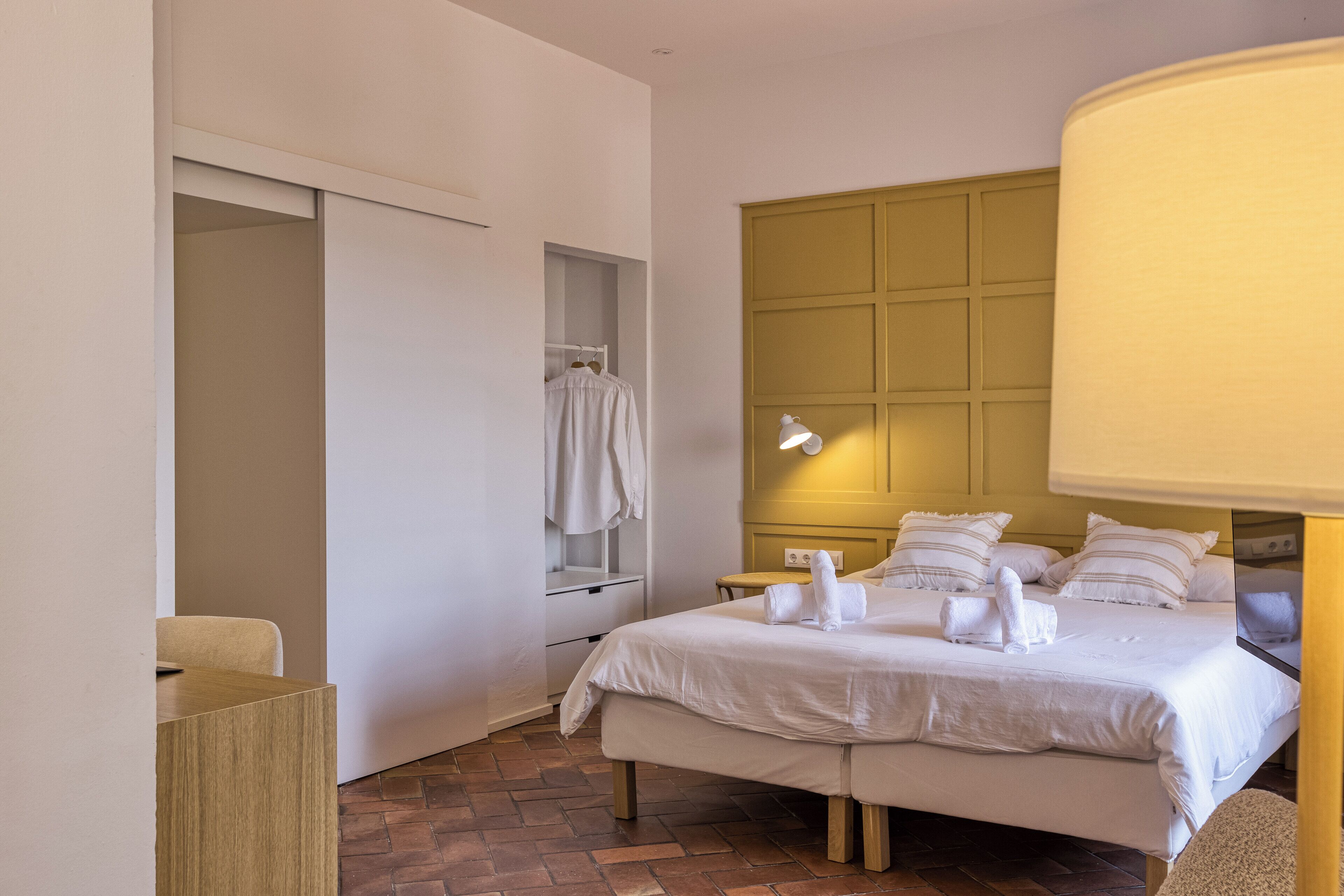 Une chambre d’hôtel avec un grand lit, une table de chevet, une lampe, une armoire et un miroir.