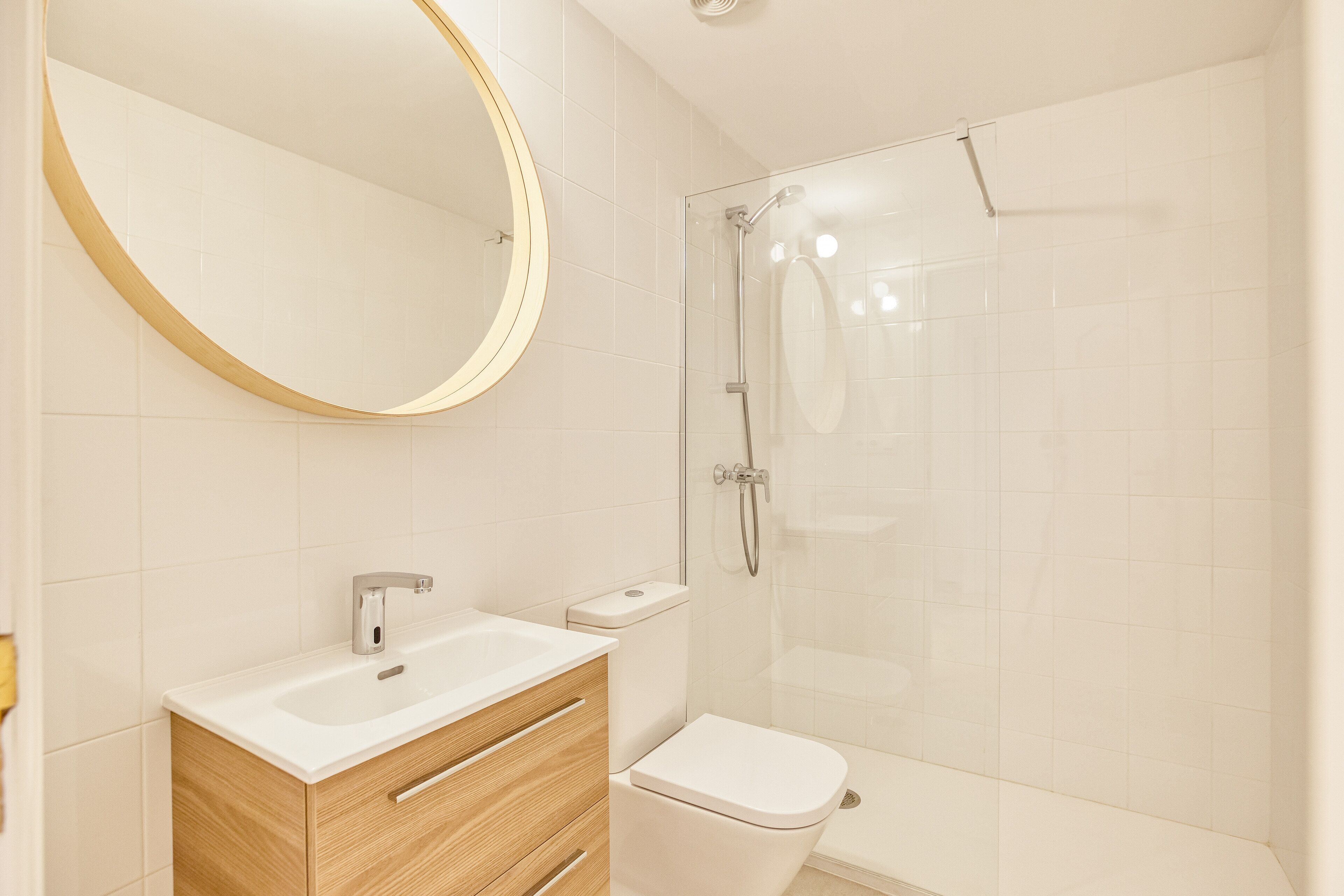 Une salle de bain moderne avec un lavabo blanc, un meuble-lavabo en bois, des toilettes et une douche à parois de verre.