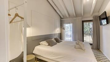 Un dormitorio con una cama grande, una mesita de noche, un armario, un espejo, un televisor montado en la pared y una ventana con cortinas.