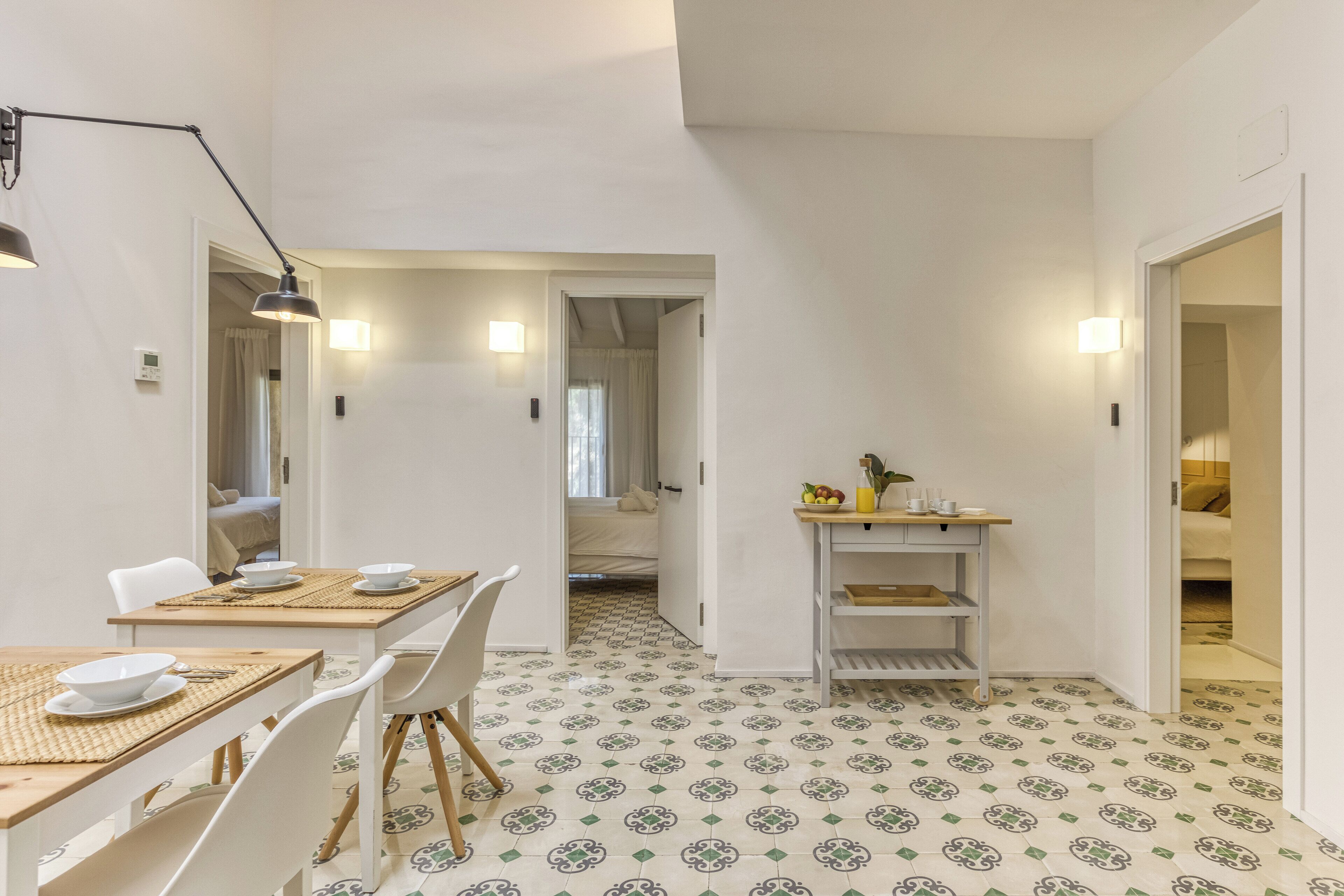 A dining area with a table set for two, a shelf with kitchen items, and a patterned floor.