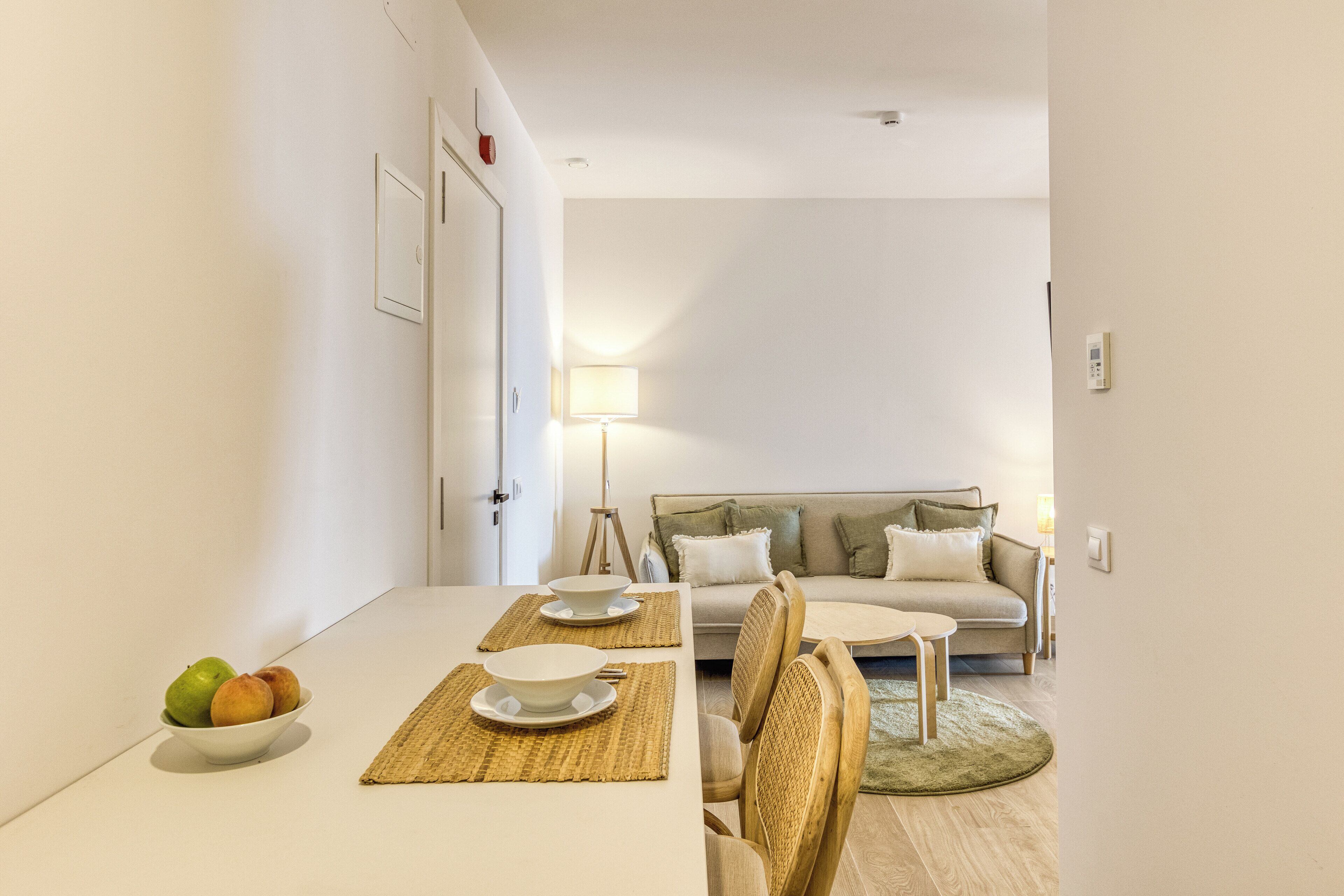 Un comedor con una mesa dispuesta para dos, un frutero y un sofá al fondo.