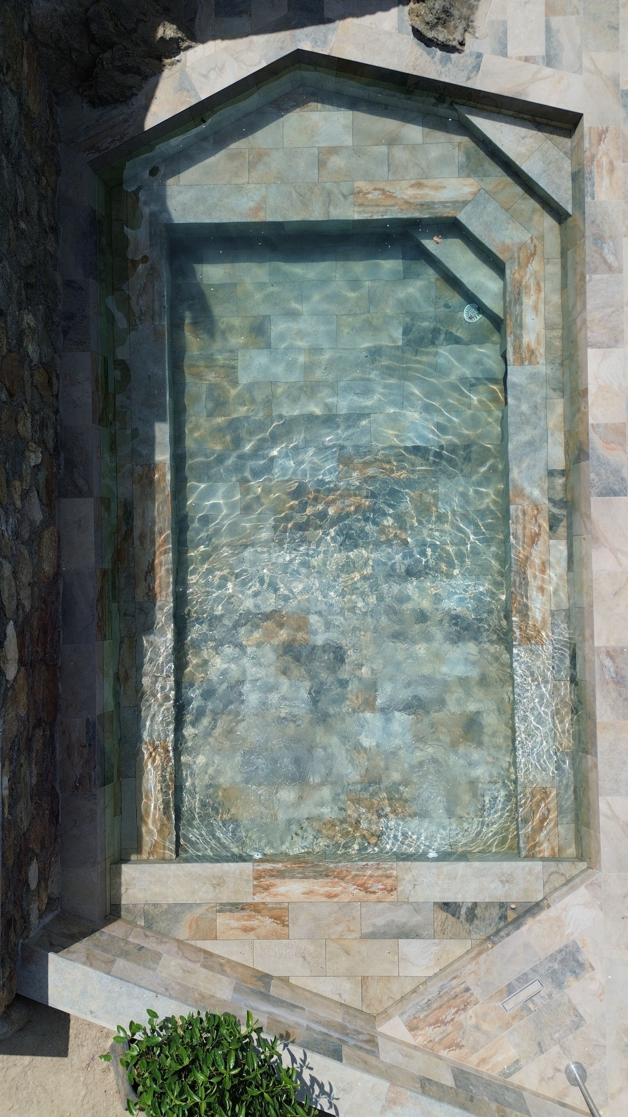 Una fuente rectangular de aguas claras, rodeada de piedra, ubicada en un área empedrada con escalones que la conducen.