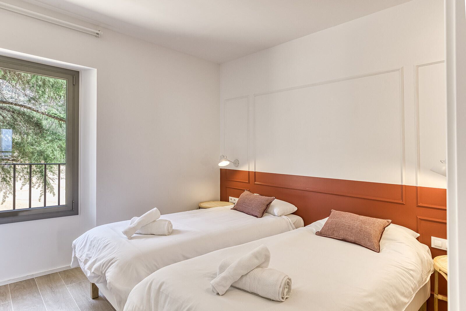 Habitación de hotel con dos camas, ventana con vista a árboles y cabecero de madera.