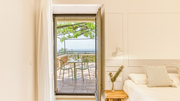 A bedroom with a bed, a bedside table, and a view of an outdoor patio with chairs and a table. - Mas Cusi (Palau-Saverdera)