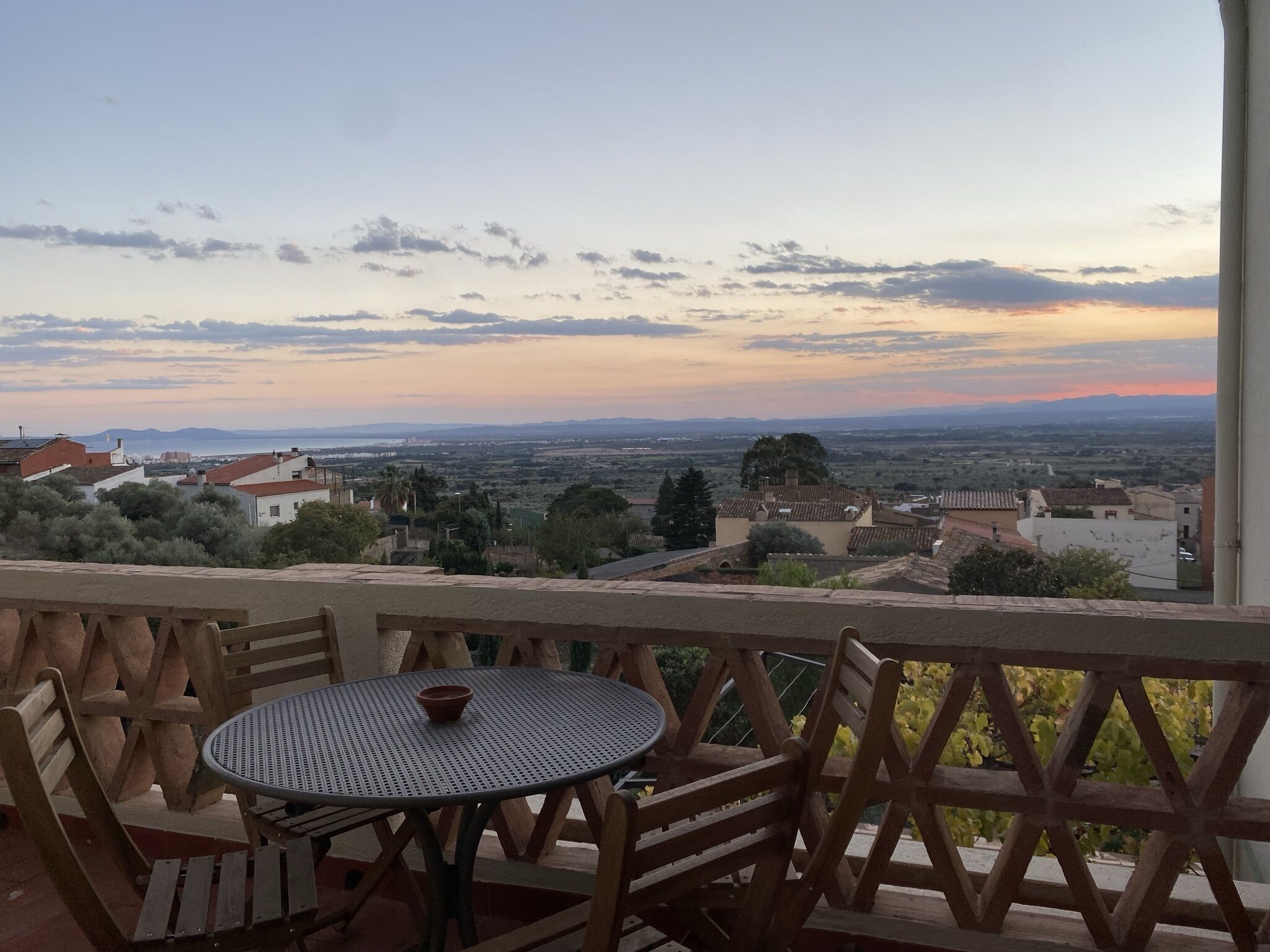 Una terraza con una mesa redonda y sillas, con vista a un paisaje pintoresco de un pueblo con edificios y árboles.