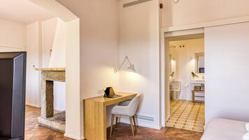 Une chambre d’hôtel moderne avec une cheminée en pierre, un bureau avec un ordinateur portable, une chaise grise et un lit.